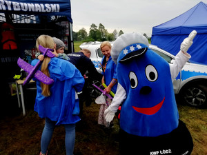 Komisarz Błysk przed policyjnym namiocie, w tle osoby odwiedzające policyjne stoisko