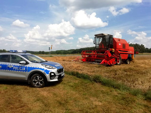 radiowóz stojący na polu, obok stoi kombajn