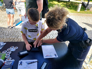policjantka pomaga chłopcu zrobic odcisk linii papilarnych