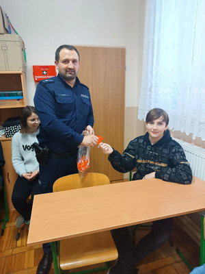 policjant rozdaje elementy odblaskowe w Szkole Podstawowej na terenie Mierzyna
