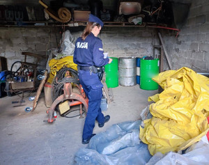 policjantka wykonuje czynności w pomieszczeniach garażu, gdzie ujawniono beczki z paliwem pochodzące z kradzieży