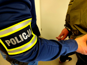 policjant trzymający zatrzymanego, który ma założone kajdanki