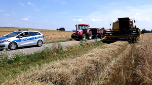 Policyjny radiowóz zaparkowany przy polu, obok rolniczy kombajn i ciągnik.