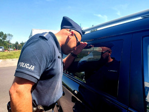 policjant zaglądający przez szybę do wnętrza zamkniętego samochodu.