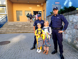 Na zdjęciu widać policjantkę i policjanta wraz z dwójka dzieci pod jedną ze szkół podstawowych.