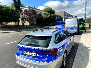 Na zdjęciu widać dwa radiowozy oraz policjanta podczas kontroli pojazdu przy jednej ze szkół podstawowych.