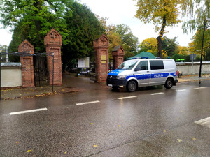 Policyjny radiowóz przed bramą cmentarną.