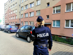 Policjantka stojąca przed blokiem mieszkalnym.