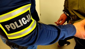 rękaw policjanta i widoczne ręce zatrzymanego, na które są założone kajdanki.