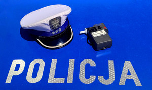 Napis policja, czapka policjanta z wydziału ruchu drogowego oraz urządzenie do badania trzeźwości.