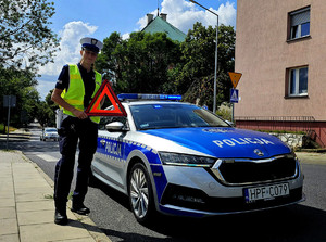 Policjant trzymający trójkąt ostrzegawczy.