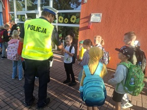 Policjanci wraz z przedstawicielem WORD podczas przekazywania elementów odblaskowych dzieciom przed wejściem do szkoły w Gomulinie.