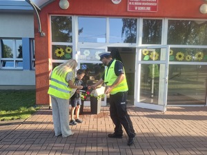 Policjanci wraz z przedstawicielem WORD podczas przekazywania elementów odblaskowych dzieciom przed wejściem do szkoły w Gomulinie.