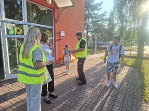 Policjanci wraz z przedstawicielem WORD podczas przekazywania elementów odblaskowych dzieciom przed wejściem do szkoły w Gomulinie.