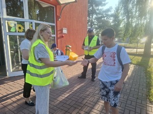 Policjanci wraz z przedstawicielem WORD podczas przekazywania elementów odblaskowych dzieciom przed wejściem do szkoły w Gomulinie.