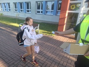 Policjanci wraz z przedstawicielem WORD podczas przekazywania elementów odblaskowych dzieciom przed wejściem do szkoły w Gomulinie.