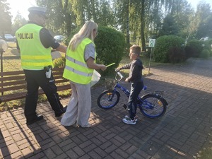 Policjanci wraz z przedstawicielem WORD podczas przekazywania elementów odblaskowych dzieciom przed wejściem do szkoły w Gomulinie.