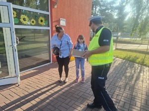Policjanci wraz z przedstawicielem WORD podczas przekazywania elementów odblaskowych dzieciom przed wejściem do szkoły w Gomulinie.