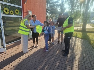 Policjanci wraz z przedstawicielem WORD podczas przekazywania elementów odblaskowych dzieciom przed wejściem do szkoły w Gomulinie.