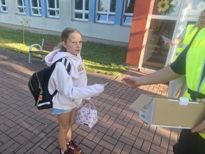 Policjanci wraz z przedstawicielem WORD podczas przekazywania elementów odblaskowych dzieciom przed wejściem do szkoły w Gomulinie.