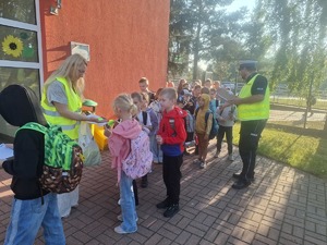 Policjanci wraz z przedstawicielem WORD podczas przekazywania elementów odblaskowych dzieciom przed wejściem do szkoły w Gomulinie.