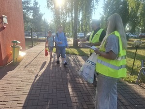 Policjanci wraz z przedstawicielem WORD podczas przekazywania elementów odblaskowych dzieciom przed wejściem do szkoły w Gomulinie.