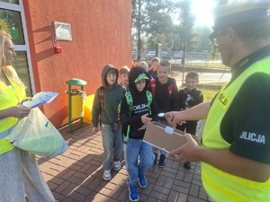 Policjanci wraz z przedstawicielem WORD podczas przekazywania elementów odblaskowych dzieciom przed wejściem do szkoły w Gomulinie.
