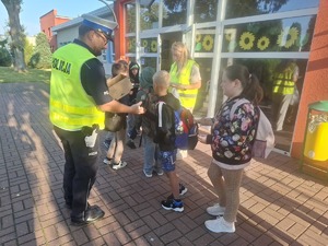 Policjanci wraz z przedstawicielem WORD podczas przekazywania elementów odblaskowych dzieciom przed wejściem do szkoły w Gomulinie.
