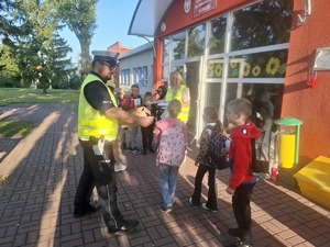 Policjanci wraz z przedstawicielem WORD podczas przekazywania elementów odblaskowych dzieciom przed wejściem do szkoły w Gomulinie.