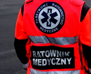 Napis ratownik medyczny umieszczony na kurtce koloru pomarańczowego.