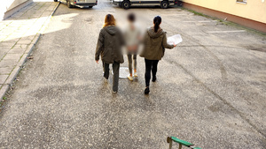 Dwie policjantki prowadzące zatrzymana kobietę przez dziedziniec komendy.