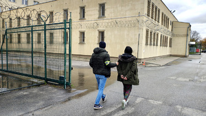 Policjant prowadzący zatrzymaną kobietę przez dziedziniec komendy.