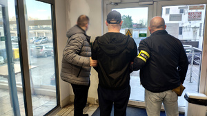 Policjant z zatrzymanym na dziedzińcu komendy.