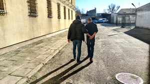 Policjant z zatrzymanym na dziedzińcu komendy.