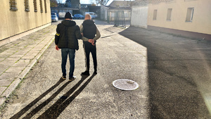 Policjant z zatrzymanym na dziedzińcu komendy.