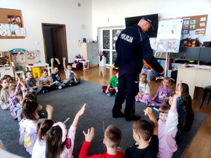 Policjant wręczający dzieciom elementy odblaskowe.