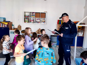 Policjant wręczający dzieciom elementy odblaskowe.