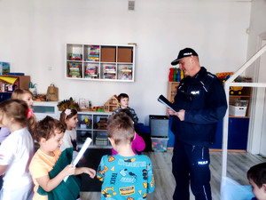Policjant wręczający dzieciom elementy odblaskowe.