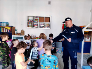 Policjant wręczający dzieciom elementy odblaskowe.