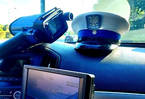 W radiowozie na podszybiu leży policyjna czapka, po lewej stronie rejestrator prędkości.