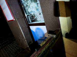 Drzwi do sklepu z wybitą szybą oraz leżący po prawej stronie młotek.