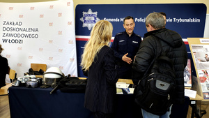 Policjant z kobietą i mężczyzną przy stoisku promocyjnym.