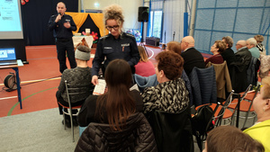 Policjantka rozdaje ulotki seniorom.