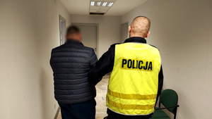 Zatrzymany mężczyzna trzymany przez policjanta.