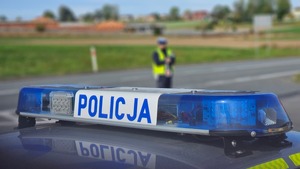 dach radiowozu z oświetleniem i napisem policja. W tle policjant drogówki.