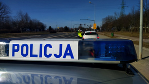 Napis policja, w tle funkcjonariusze kontrolujący pojazd.