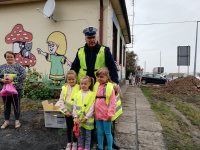 policjant z rozdaje przedszkolakom kamizelki odblaskowe
